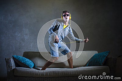 Attractive and cool happy man playing air guitar listening to music with yellow headphones holding mobile phone jumped on top of Stock Photo