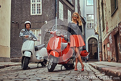 Attractive couple, a handsome man and female standing on an old street with two retro scooters. Stock Photo