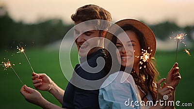 Attractive couple moving with lights in park. Guy and girl posing with sparklers Stock Photo