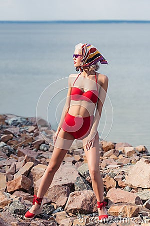 attractive elegant girl posing in red bikini and silk scarf on rocky beach Stock Photo