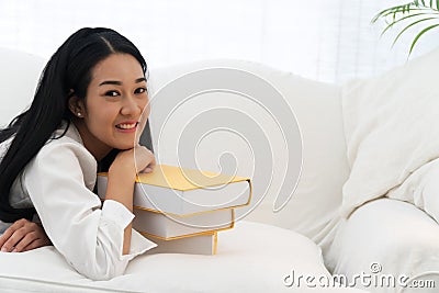 Face smile of young woman lying on white sofa with yellow stack of book looking at camera Stock Photo