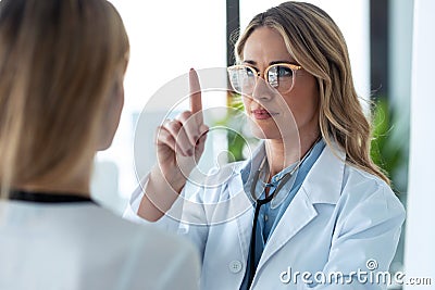 Attractive female doctor ophtalmologist checking the eye vision of beautiful young woman in consultation Stock Photo