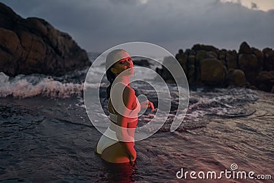 Attractive female enjoys serene night dip in ocean, red illumination enhancing beauty, travel in aquatic settings. Woman Stock Photo