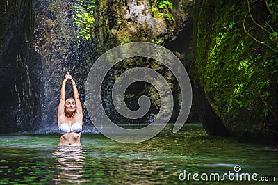 Attractive and fit tourist Caucasian woman practicing yoga exercise pose in amazing tropical exotic waterfall lagoon with green tu Stock Photo