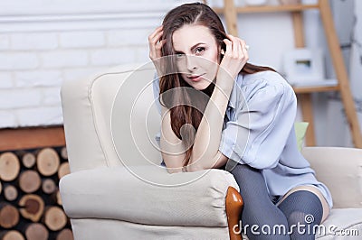 An attractive flirty young brunette is sitting in a large soft chair Stock Photo