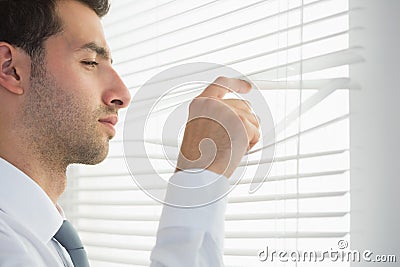 Attractive frowning businessman spying through roller blind Stock Photo