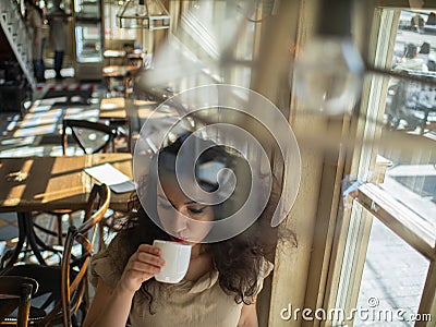 Attractive girl with curly hair sits in a cafe at the table and drinks coffee Stock Photo