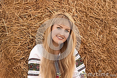 Girl with long hair in Ukrainian clother posing among the bales in the field Stock Photo