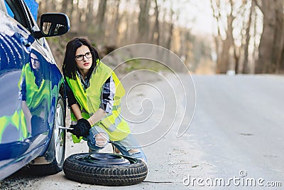 attractive girl remove wheel from car at road alone Stock Photo