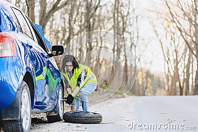 attractive girl remove wheel from car at road alone Stock Photo