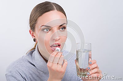 Attractive girl taking a pill with water on light background Stock Photo