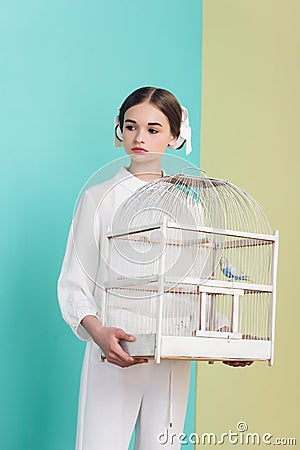 attractive girl in trendy white outfit with parrot in cage on turquoise Stock Photo