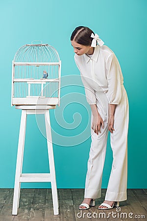 attractive girl in white looking at parrot in cage Stock Photo