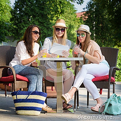 Attractive girlfriends enjoying cocktails and using wireless connection on digital tablet Stock Photo