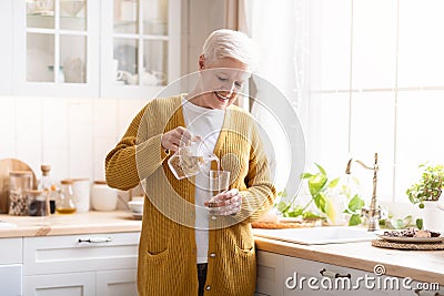 Attractive grandmother pouring water into glass in kitchen at home Stock Photo