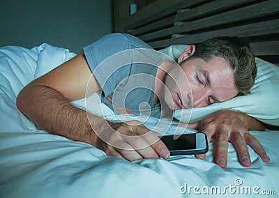 Attractive and handsome tired man on his 30s or 40s in bed sleeping peacefully and relaxed at night holding mobile phone in intern Stock Photo