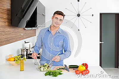 Attractive happy man making vegetarian salad on the kitchen Stock Photo