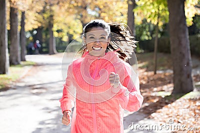 Attractive and happy runner woman in Autumn sportswear running and training on jogging outdoors workout in city park Stock Photo