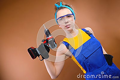 Attractive harsh young woman in overalls overalls and goggles with a screwdriver in her hand on a brown background Stock Photo