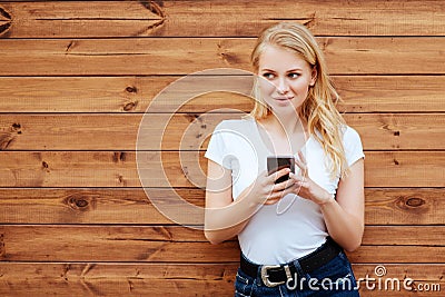 Attractive laughing female standing with mobile phone against wooden wall background Stock Photo