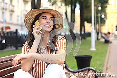 Attractive laughing woman talking on cellphone while sitting on bench outdoors Stock Photo