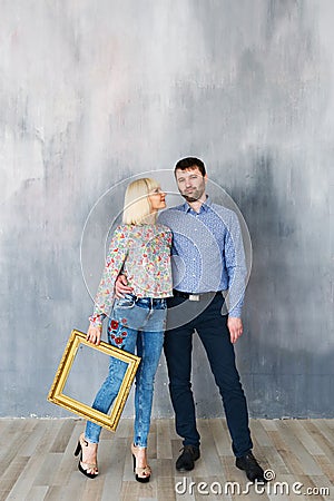 Attractive loving couple are standing near the texture wall, look at the camera and smiling. Stock Photo