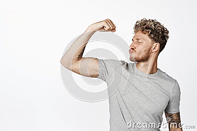 Attractive macho man kisses his muscle, flexing biceps as bragging physical form, strengths in arms, workout result Stock Photo