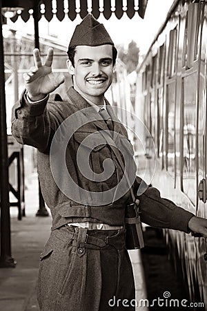 Handsome male British soldier in WW2 vintage uniform at train station next to train, waving and smiling Stock Photo