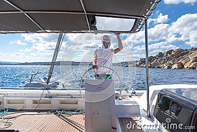 Attractive male skipper navigating the fancy catamaran sailboat on sunny summer day on calm blue sea water. Stock Photo