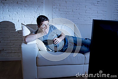 Attractive man at home lying on couch at living room watching tv looking surprised in shock Stock Photo