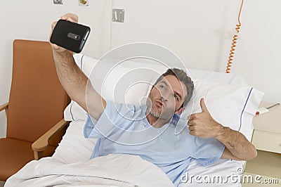 Attractive man lying on bed hospital clinic holding mobile phone taking self portrait selfie photo Stock Photo