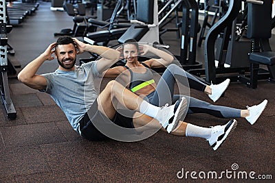 Attractive man and woman working in pairs performing sit ups in gym Stock Photo
