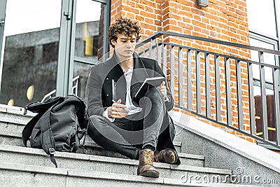 Attractive man writing notes in his notepad on red bricked building steps Stock Photo