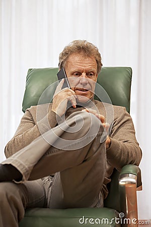 Attractive mature man talking on smartphone in a chair in a living room Stock Photo