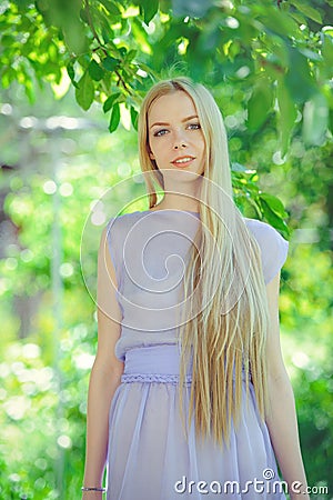 Attractive modest young girl with blond hair and natural make-up in purple dress outdoors, tenderness and softness on nature Stock Photo