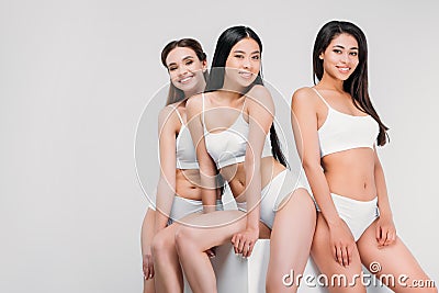 attractive multiethnic girls in underwear posing on white cube Stock Photo