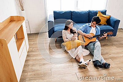 Attractive new marriage man and woman sit on the floor enjoy singing and playing guitar in the living room at the new home. Stock Photo