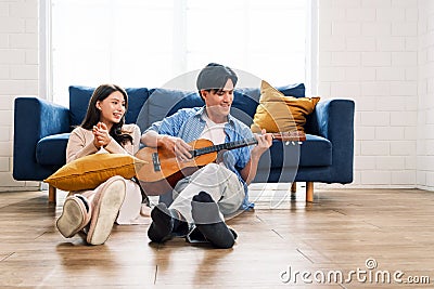 Attractive new marriage man and woman sit on the floor enjoy singing and playing guitar in the living room at the new home. Stock Photo