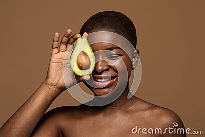 Attractive Nude Black Female With Clean Skin Covering Eye With Avocado Half Stock Photo