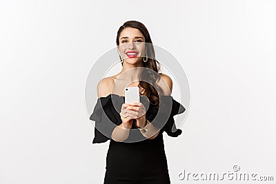 Attractive party girl taking photo on smartphone, make photograph on mobile phone camera, standing in black dress over Stock Photo