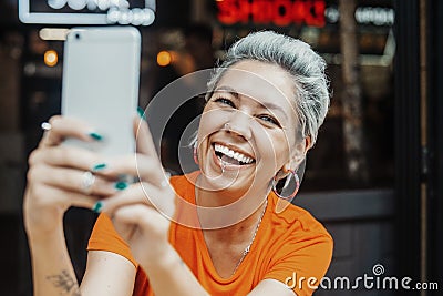 Attractive positive blonde woman in orange T-shirt making selfie at cafe Stock Photo