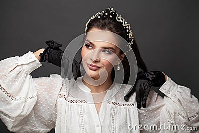 Attractive positive brunette model woman wearing black headband and pearls earring on black background portrait Stock Photo