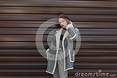 Attractive pretty young woman in trendy black T-shirt in a vintage checkered coat in gray stylish pants poses near a metal wall Stock Photo