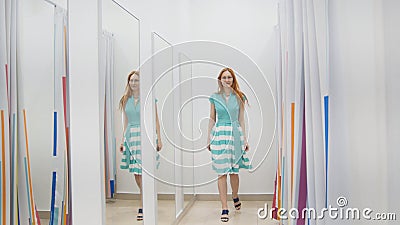 Attractive red hair girl chooses green dress near mirror in fitting room at store Stock Photo