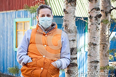 Attractive Russian woman wearing safety mask standing against rural timber house, self-isolation in nature Stock Photo