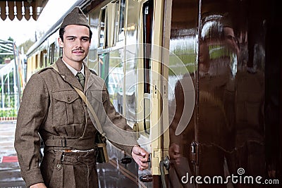 Handsome and sad male British soldier in WW2 vintage uniform at train station next to locomotive train. Stock Photo