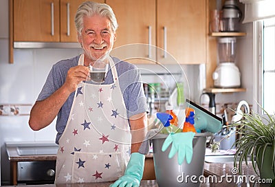 An attractive senior man has finished the housework and has a break with a coffee. Close to him a plastic bucket with items for Stock Photo