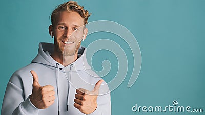 Attractive smiling bearded man in hoodie wear wireless earphones keep thumbs up near place for advertisement or Stock Photo