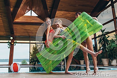 Attractive smiling slim female friends wearing swimsuits holding inflatable lounge posing in spa and wellness center Stock Photo