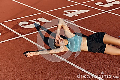 Attractive smiling sporty girl in sportswear happily lying on runner track while resting after workout on stadium Stock Photo